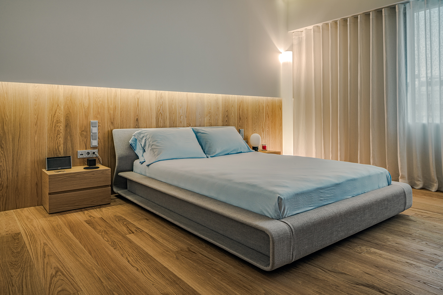 Bed headboard finished in vertically grained wood veneer, coordinated with the timber flooring, paired with two-drawer bedside tables